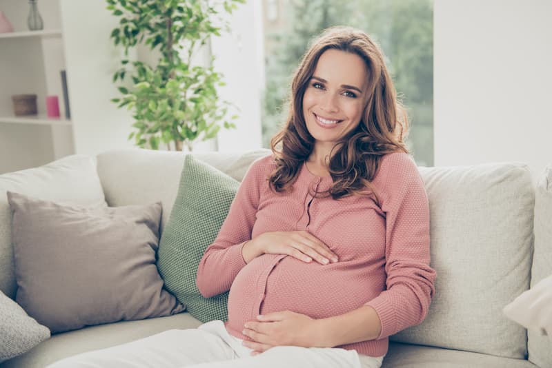 Eine schwangere Frau sitzt Zuhause auf dem Sofa, denn sie ist im Mutterschutz