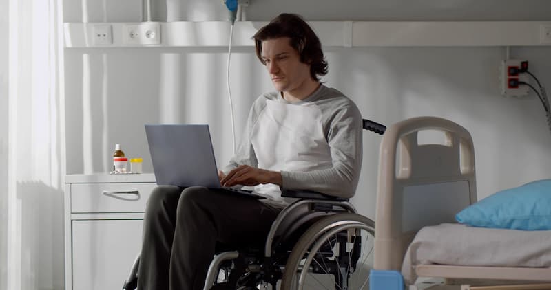 Ein Mann sitzt im Rollstuhl im Krankenhaus und informiert sich über das Krankengeld