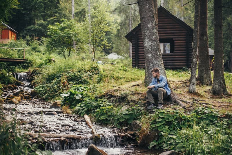 Ein Mann vor einer Hütte im Wald, er möchte Aussteiger werden