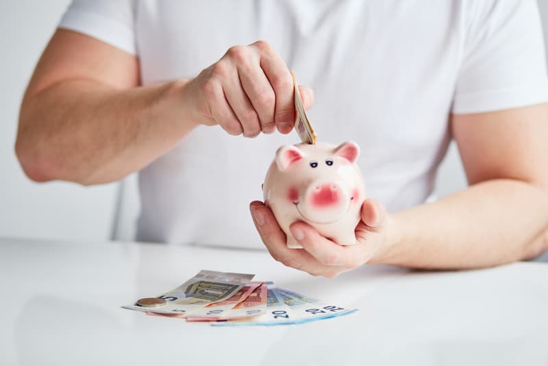 Ein Mann wirft Geld in ein Sparschwein, was ist Frugalismus?