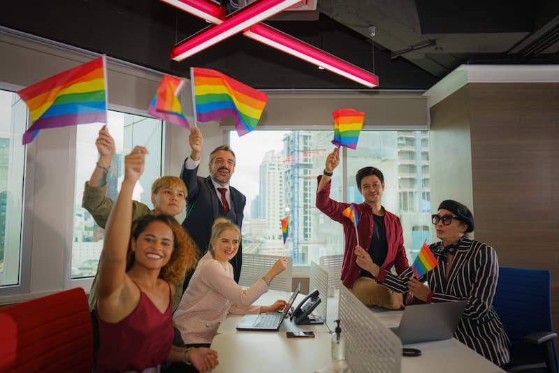 Mehrere Menschen schwenken Regenbogenflaggen im Büro, was ist Toleranz?