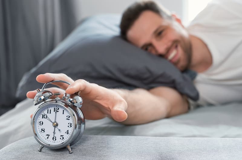 Ein Mann drückt auf den Wecker, wie kann man frühes aufstehen lernen?