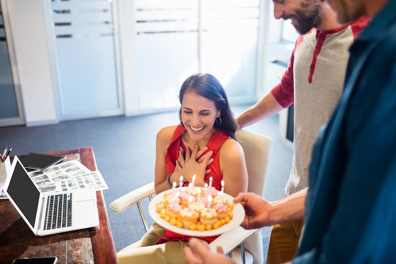 Eine Frau erhält einen Kuchen, welche Geburtstagswünsche für Kollegen sind angebracht?