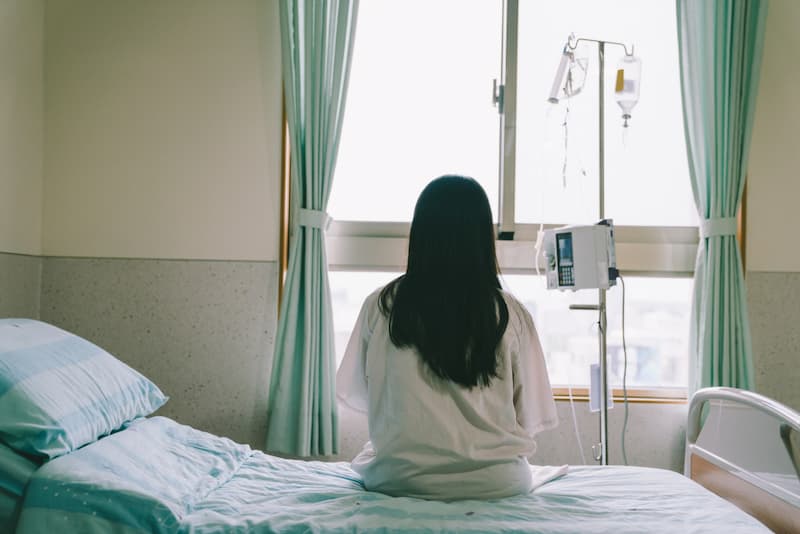 Eine Frau sitzt im Krankenhaus auf einem Bett, was bezahlt die Zusatzkrankenversicherung?