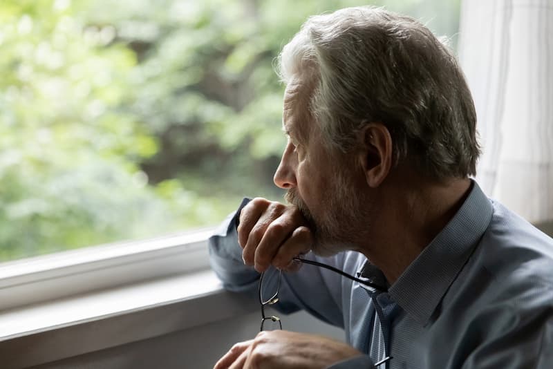 Ein älterer Mann sitzt gelangweilt am Fenster, was ist das Empty-Desk-Syndrom?