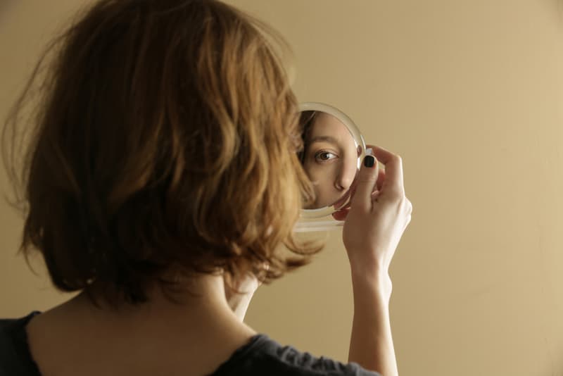 Eine Frau blickt in einen Spiegel, wie verbessert man die Selbstwahrnehmung?