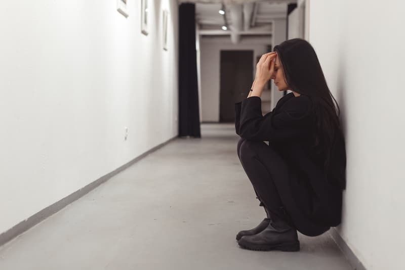 Eine Frau sitzt auf dem Boden, was führt zu einer psychischen Belastung am Arbeitsplatz?