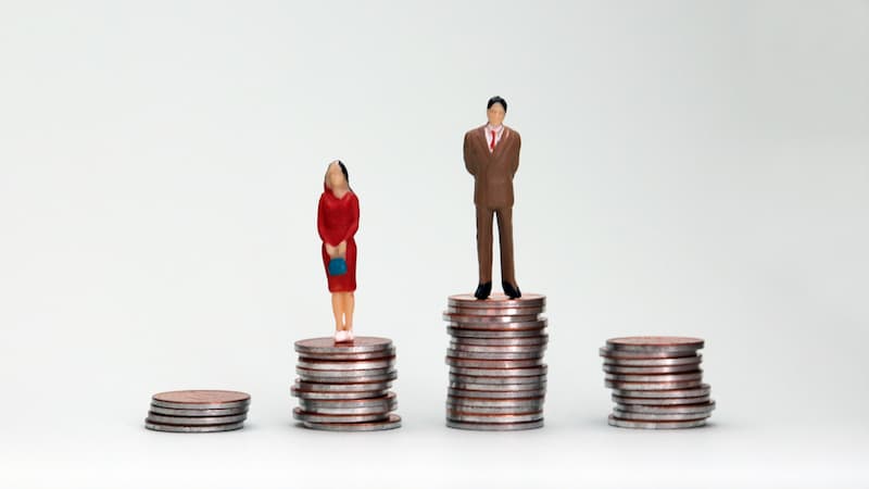 Eine Männer- und eine Frauen-Figur stehen auf unterschiedlichen Münzstapeln, was ist das Gender-Paygap?
