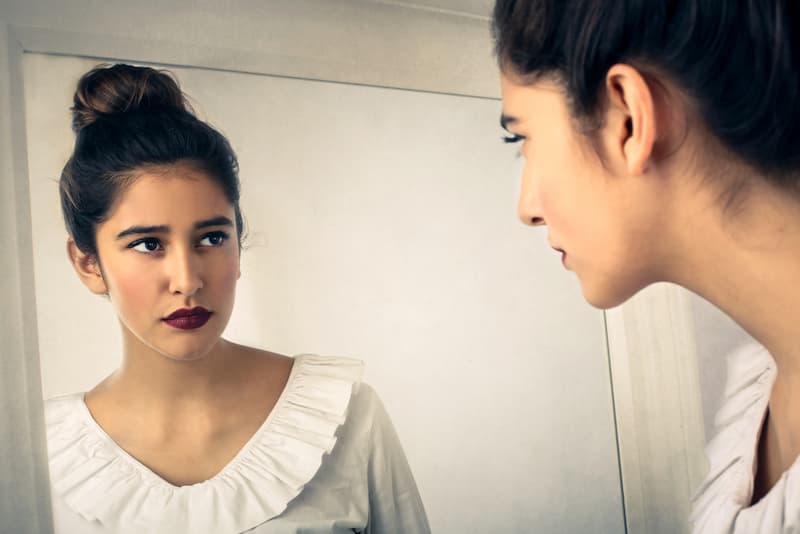 Eine Frau blickt in den Spiegel, was ist der Hindsight Bias?