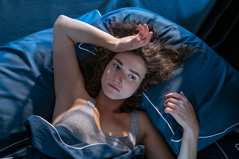 Eine Frau liegt wach im Bett, wie kann man Schlafstörungen bekämpfen?