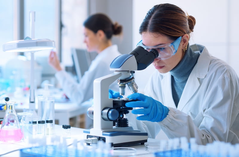 eine wissenschaftlerin uebt berufe in der forschung aus und schaut durch ein Mikroskop